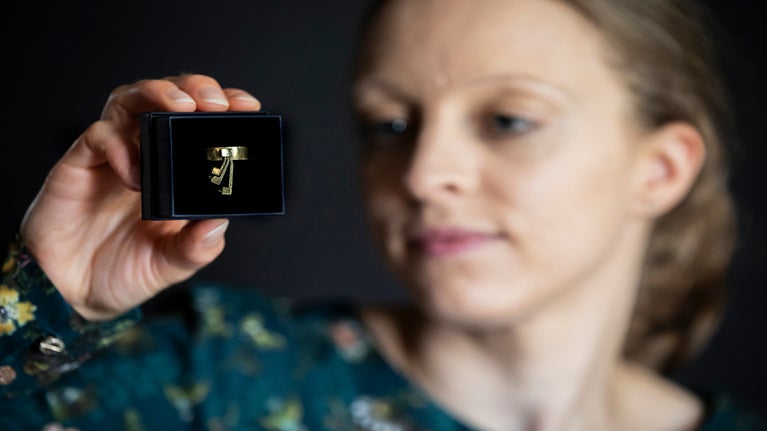 A member of the house team holding up and looking closely at a gold ring with diamond